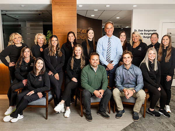The entire team at Burgmeier Dentistry smiling together with the doctors and dental assistants, all in uniform, in a comfortable and friendly environment