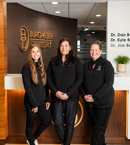 Three of our dental assistants at Burgmeier Dentistry smiling in front of the reception area