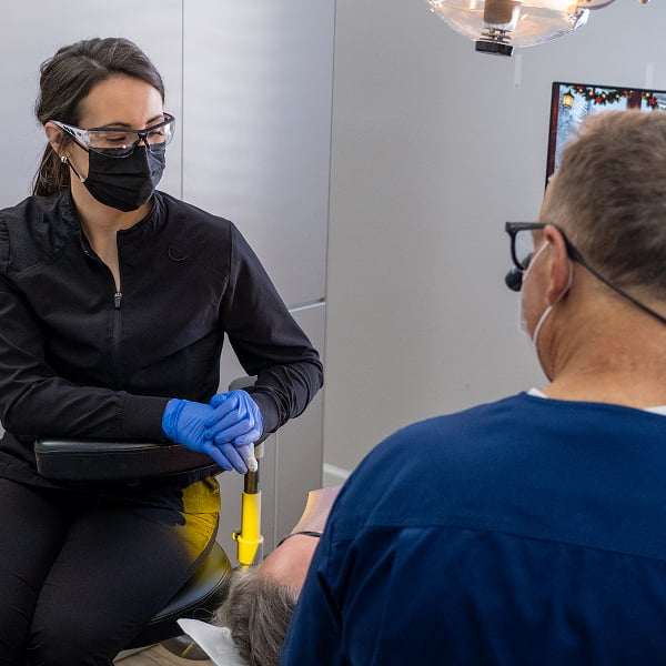 Dr. Dan Burgmeier, along with one of his dental assistants, examining the mouth of a patient who is lying back in the dental chair