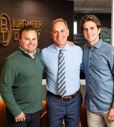 Dr. Dan Burgmeier, Dr. Kyle Burgmeier, and Dr. Joe Burgmeier smiling and hugging inside Burgmeier Dentistry