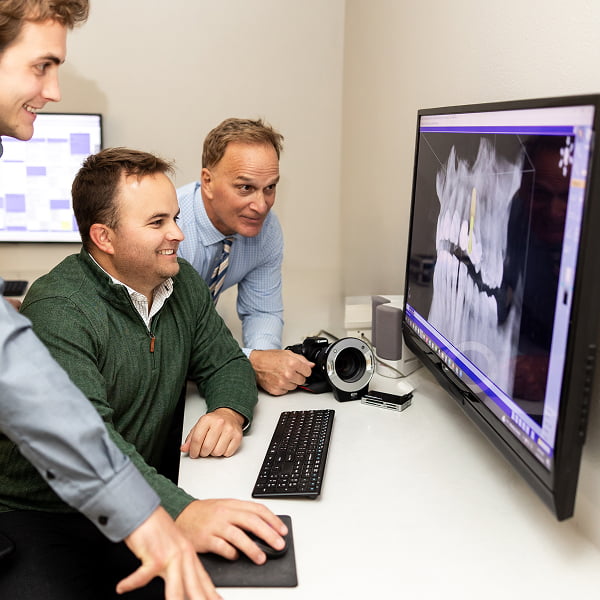 Dr. Dan Burgmeier, Dr. Kyle Burgmeier, and Dr. Joe Burgmeier smiling while reviewing dental X-rays on a monitor at Burgmeier Dentistry