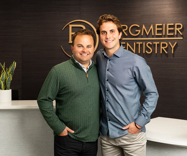 Dr. Kyle Burgmeier and Dr. Joe Burgmeier smiling in front of the front desk at Burgmeier Dentistry