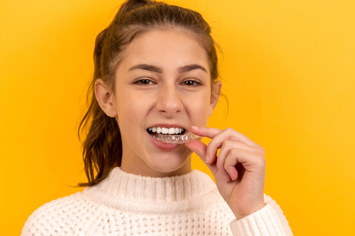 Young woman smiling and holding aligners in her hand